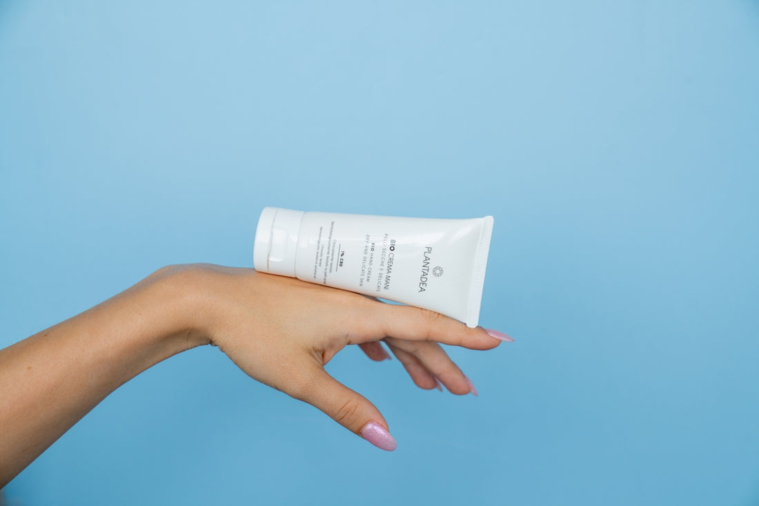 a hand holding a tube of cream against a blue background