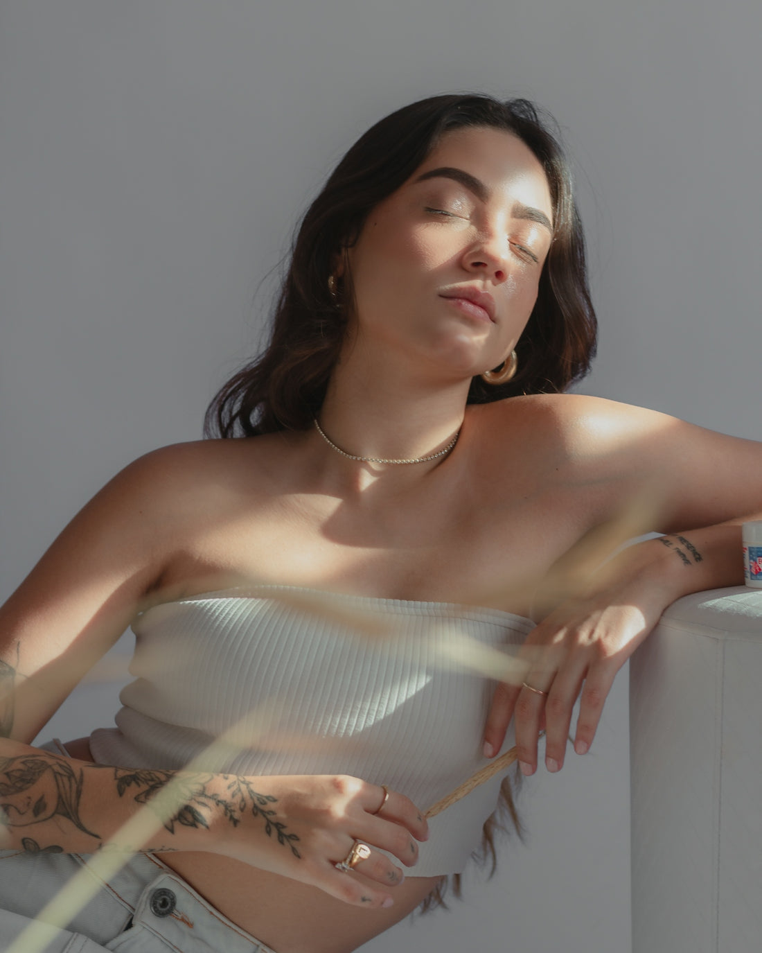 a woman wearing a white top leaning against a wall